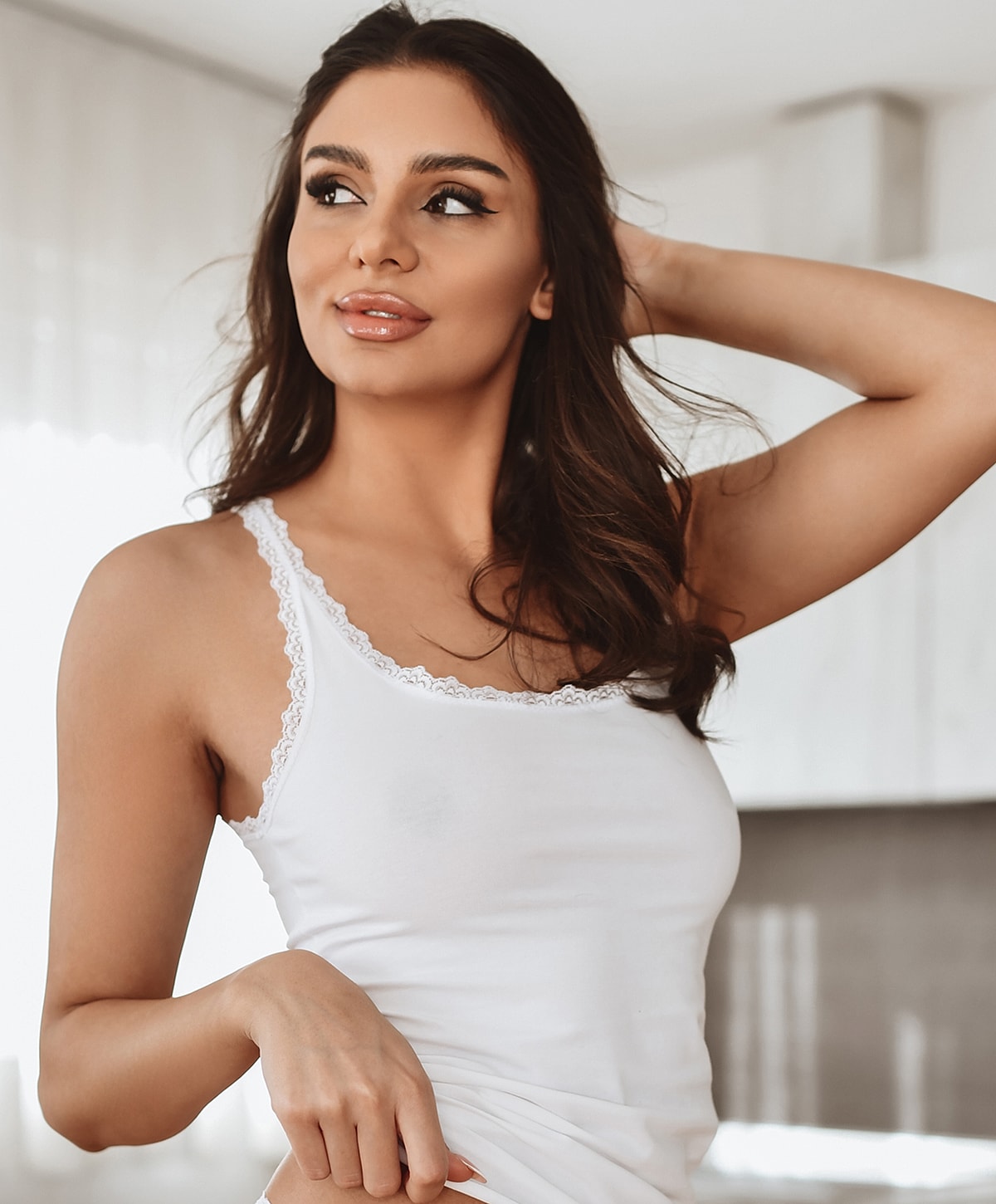Woman in white tank top, smiling indoors.