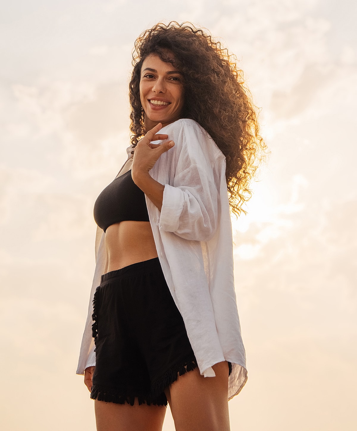 Smiling woman in summer outfit against sunset sky.