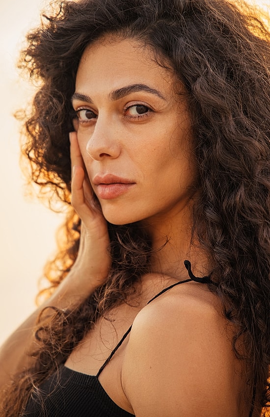 Woman with curly hair posing outdoors.
