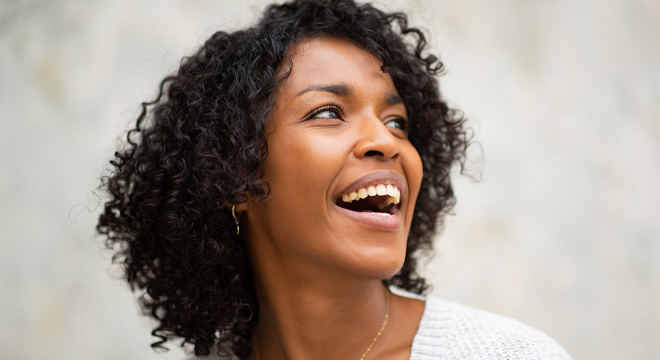 Smiling woman with curly hair in soft light.