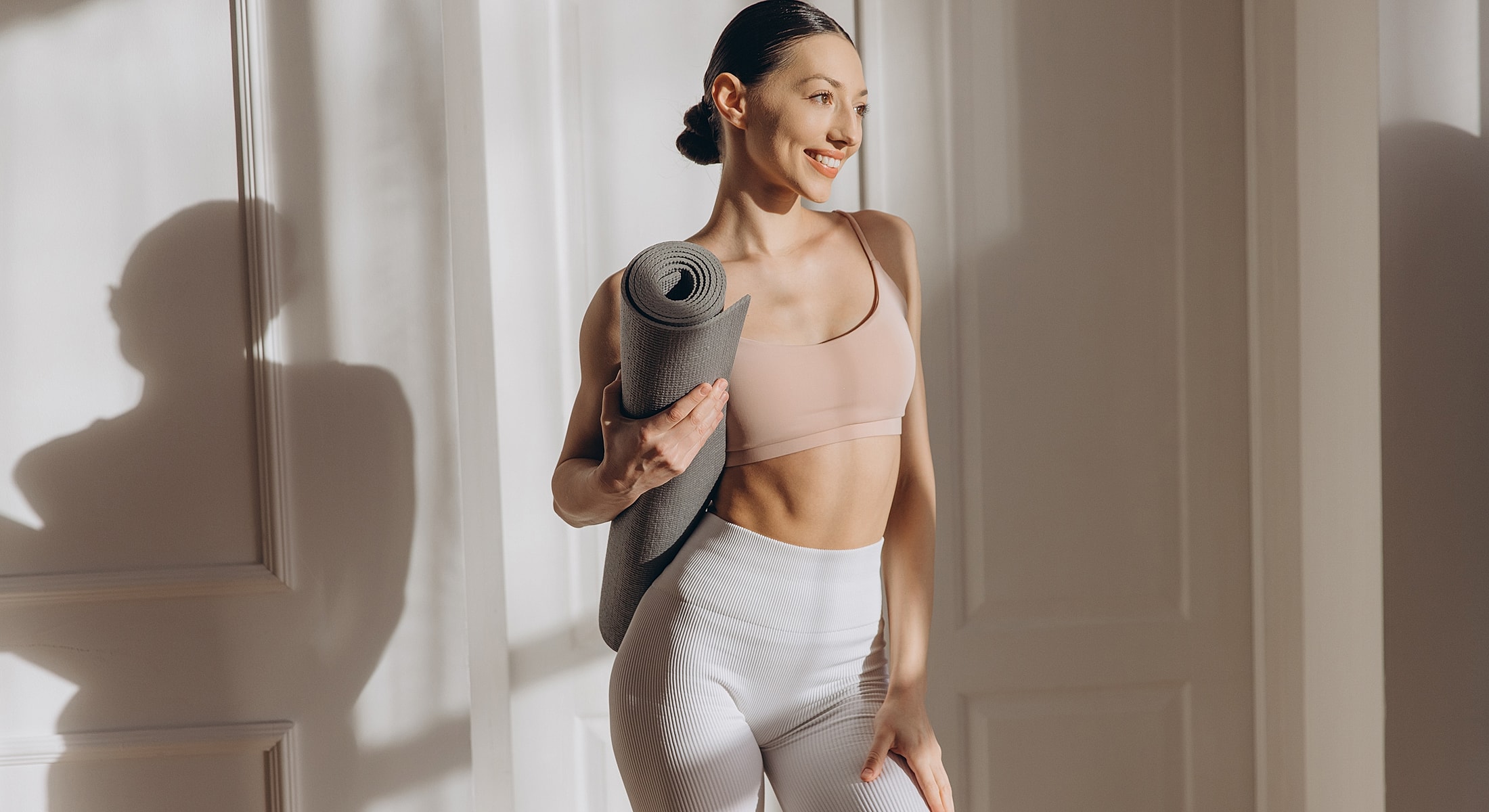 Woman holding yoga mat in bright interior.