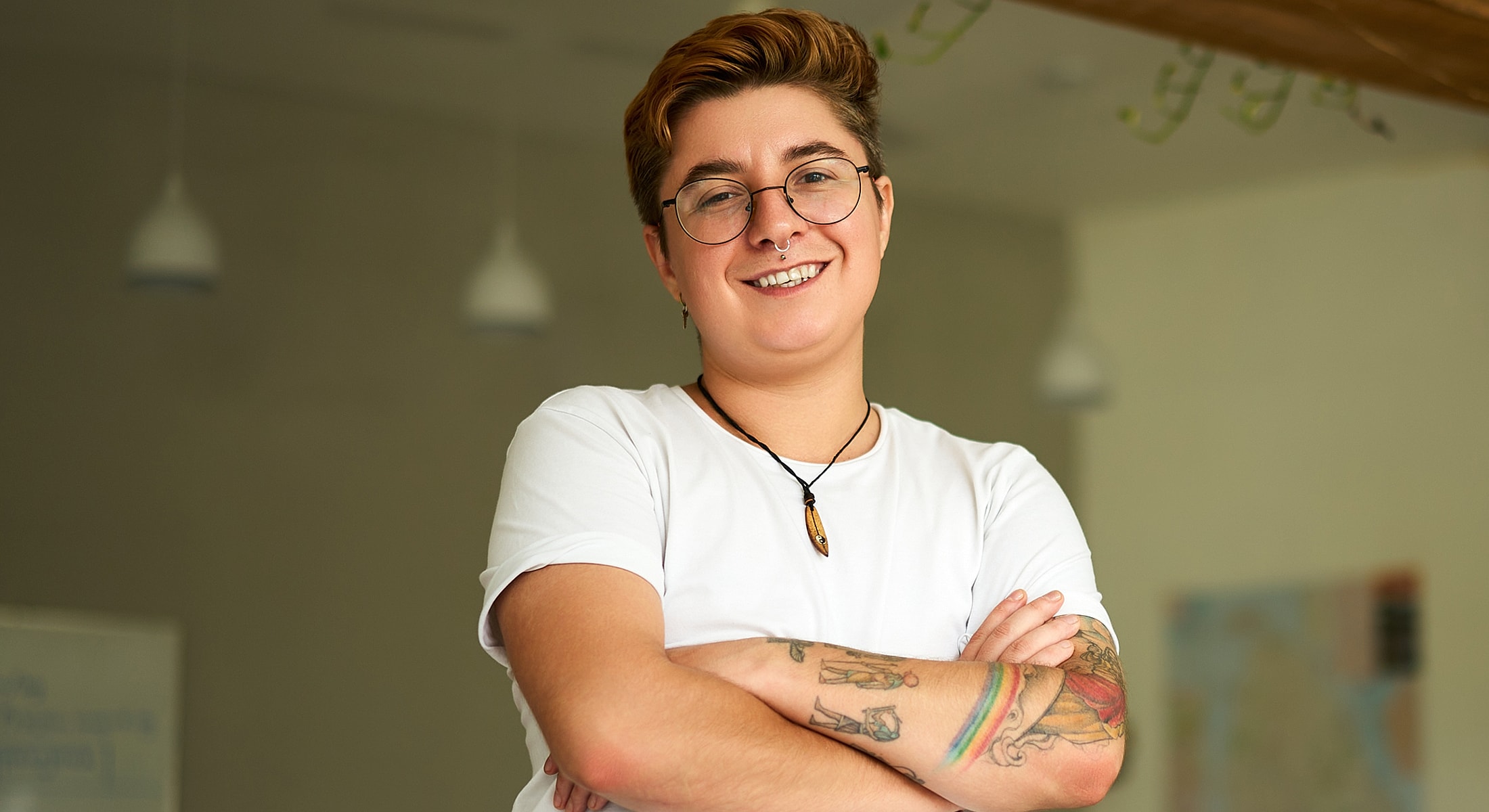 Person smiling with arms crossed, tattoos visible.